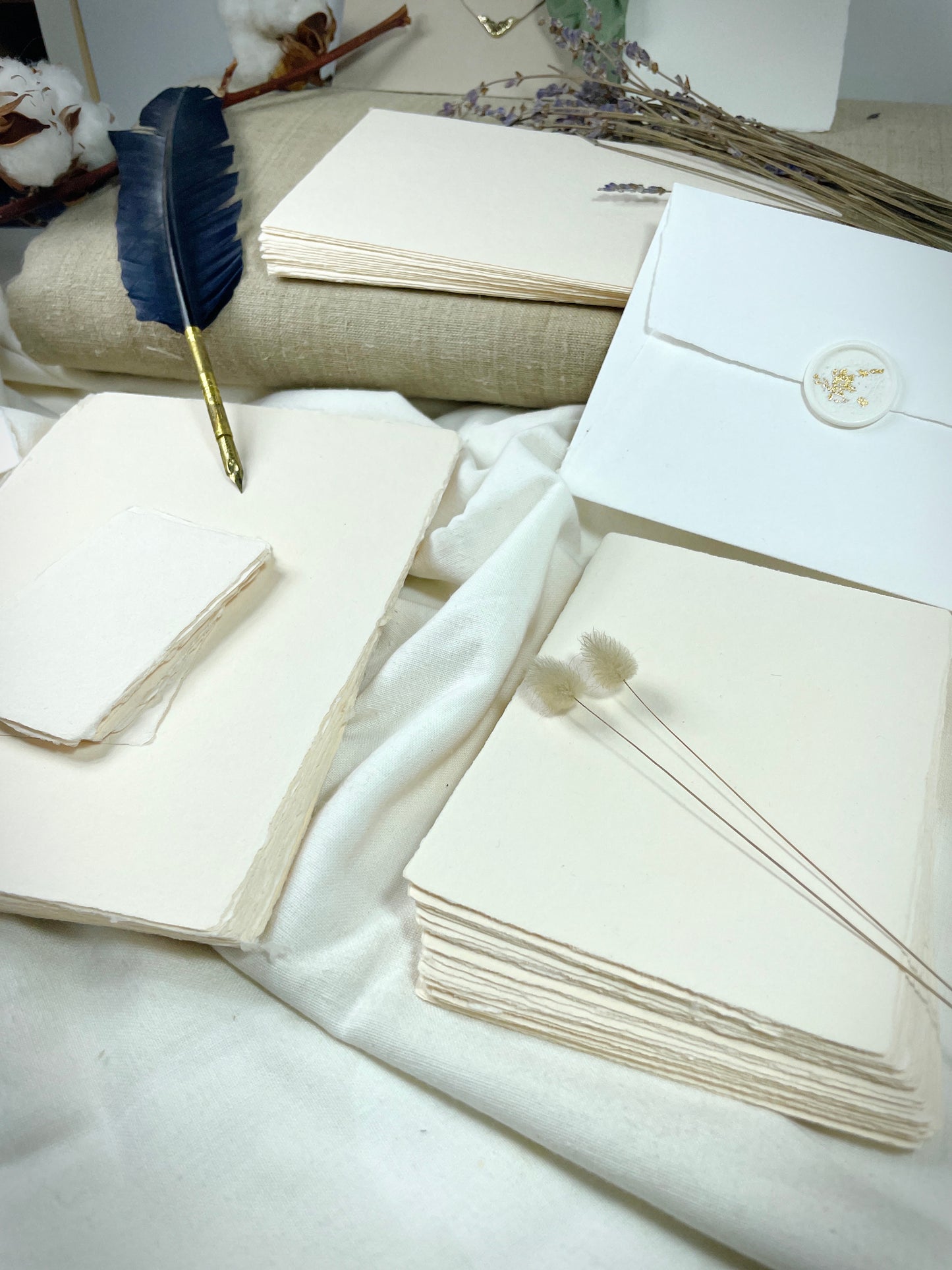 dekoratives Arrangement von cremefarbenem Büttenpapier mit Schreibfeder und Blumen