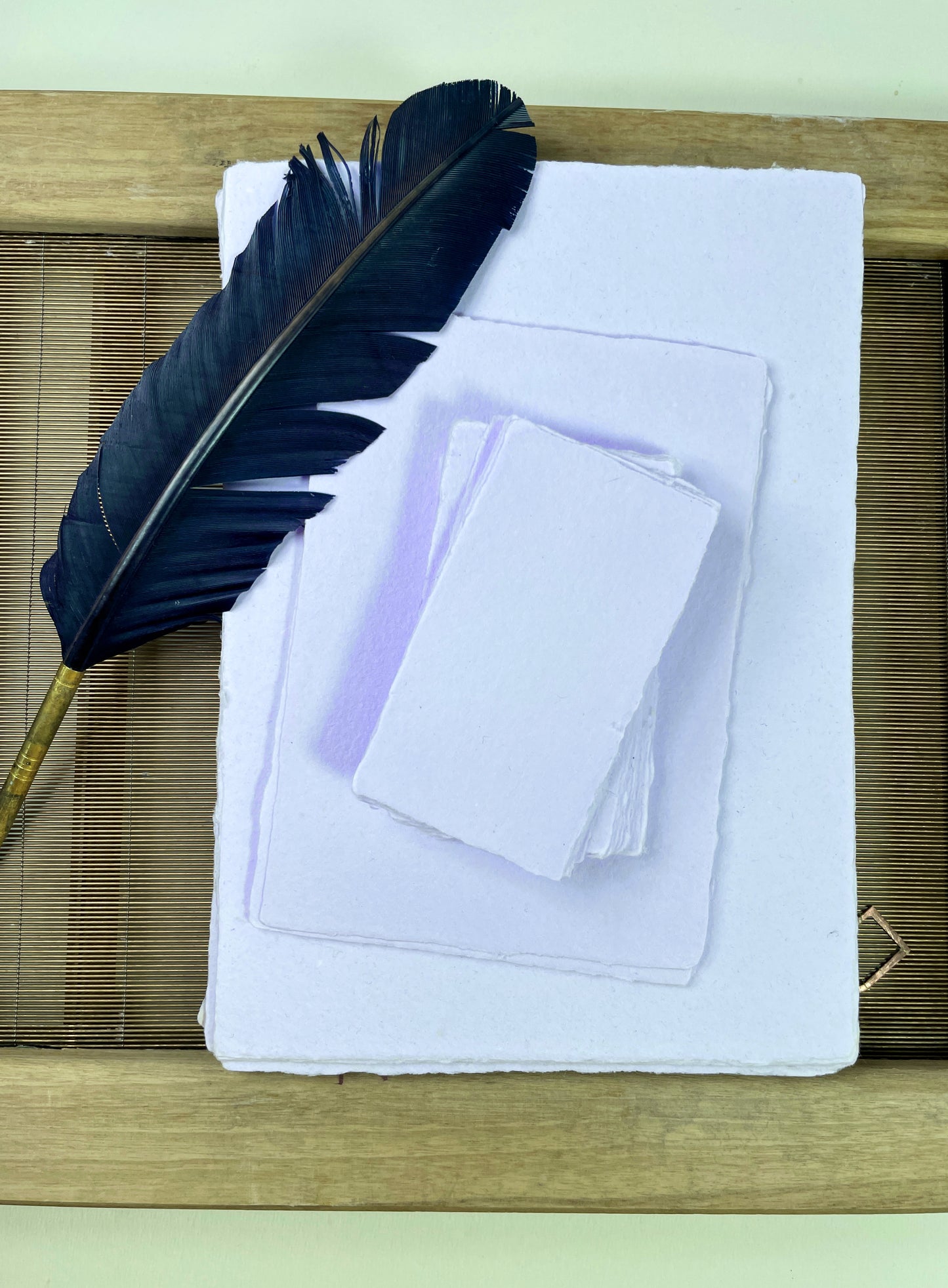 dekoratives Arrangement von violettem Büttenpapier mit Schreibfeder und Schöpfsieb