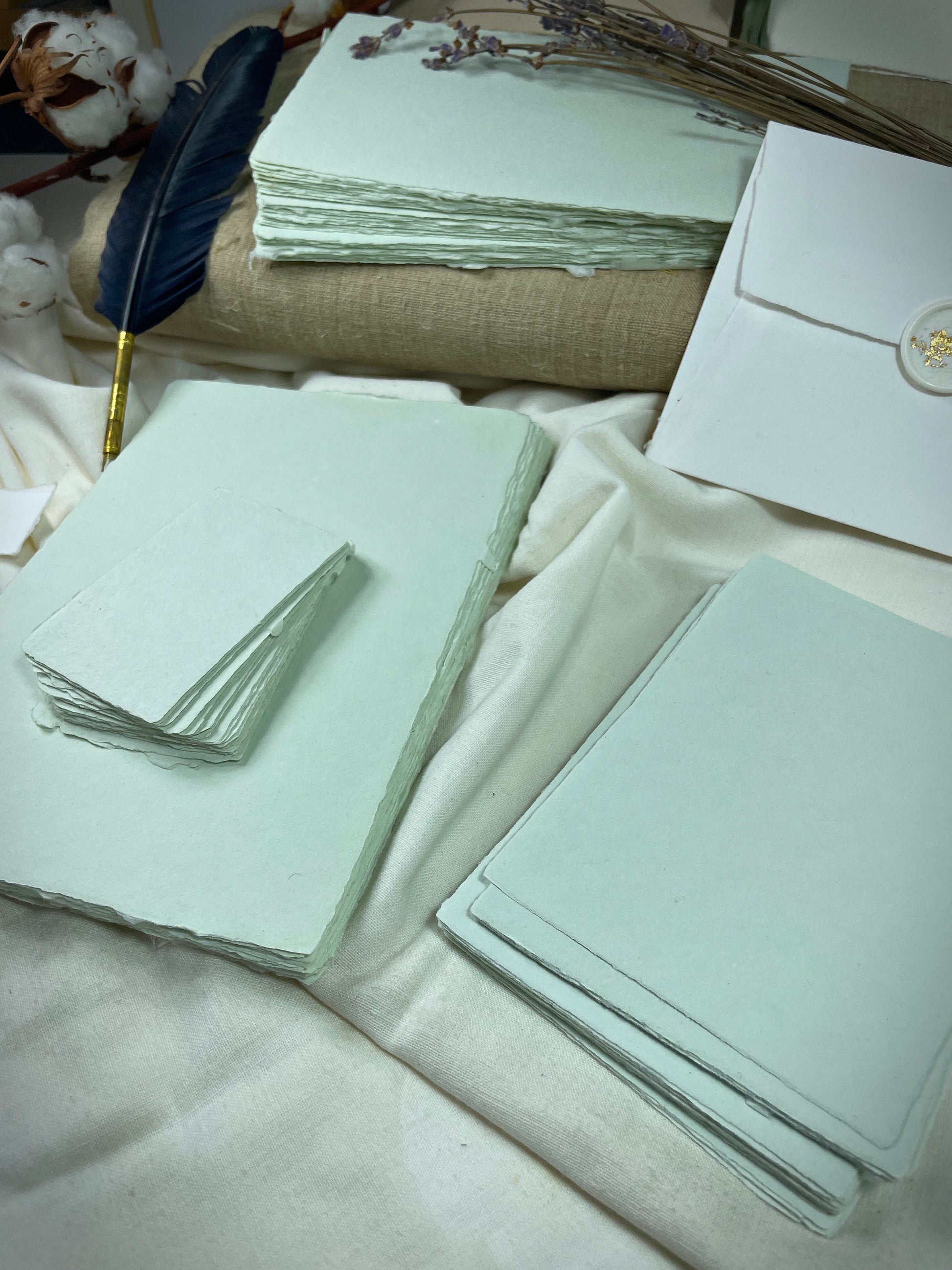 dekoratives Arrangement von mintfarbenem Büttenpapier mit Schreibfeder