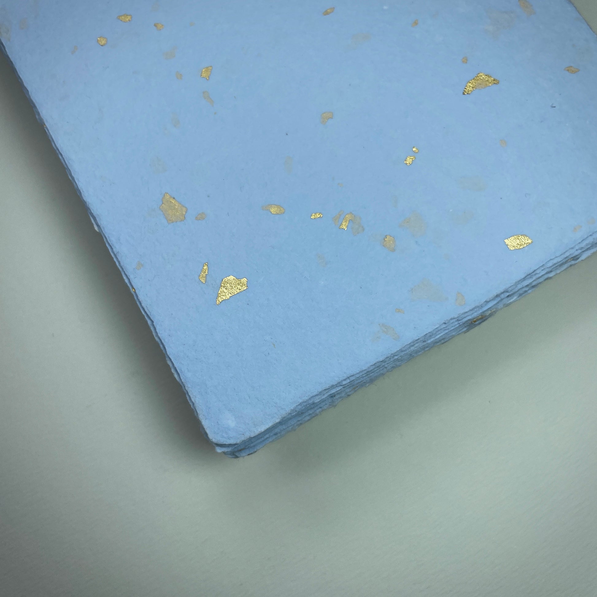 Detail eines Büttenpapiers mit eingeschöpften Goldflocken im Farbton babyblau