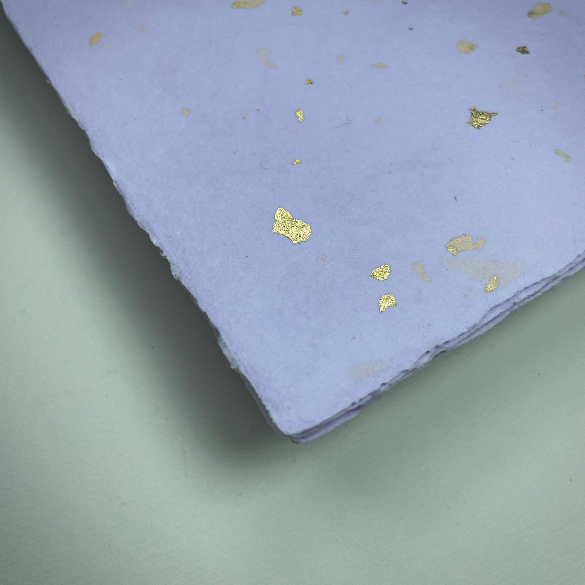 Detail eines Büttenpapiers mit eingeschöpften Goldflocken im Farbton flieder