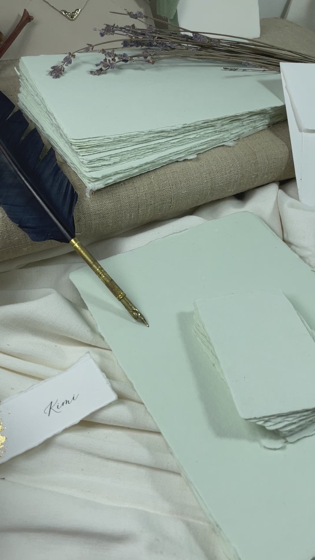 dekoratives Arrangement von mintfarbenem Büttenpapier mit Schreibfeder und Blumen