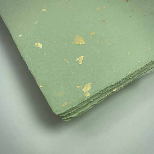 Detail eines Büttenpapiers mit eingeschöpften Goldflocken im Farbton matcha